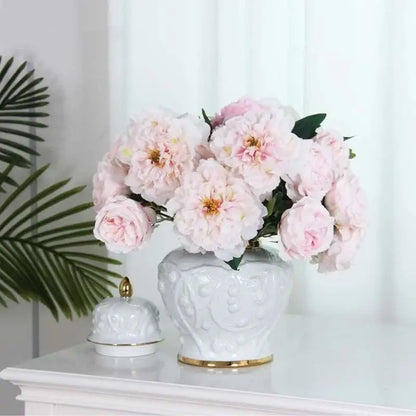 A white embossed flower ceramic ginger jar vase with gold trim holding soft pink peonies for living room storage