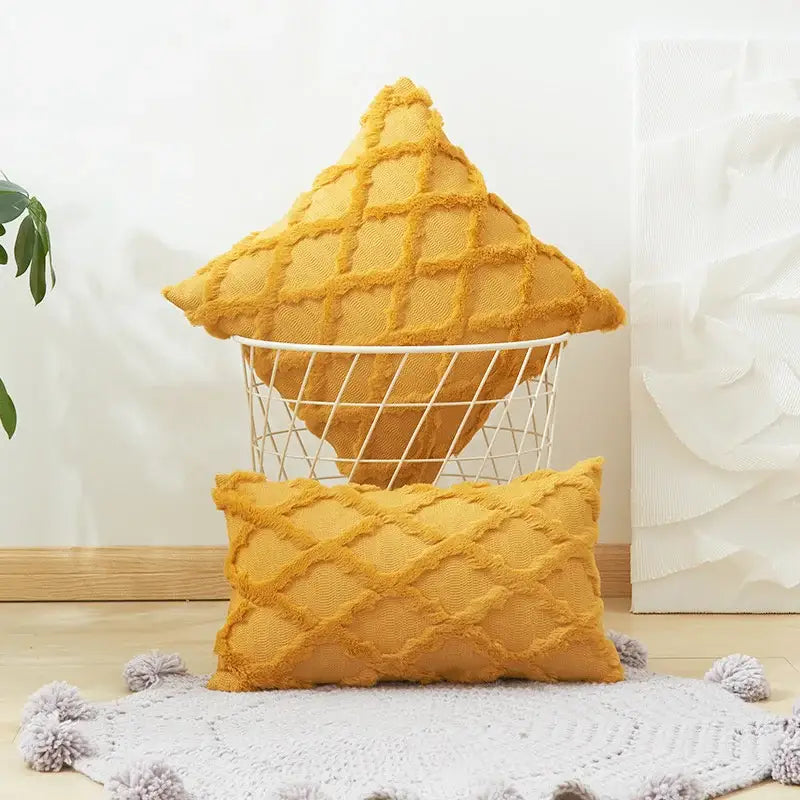 A mustard-yellow textured diamond cushion cover with embroidery and frayed edges displayed in a wire basket