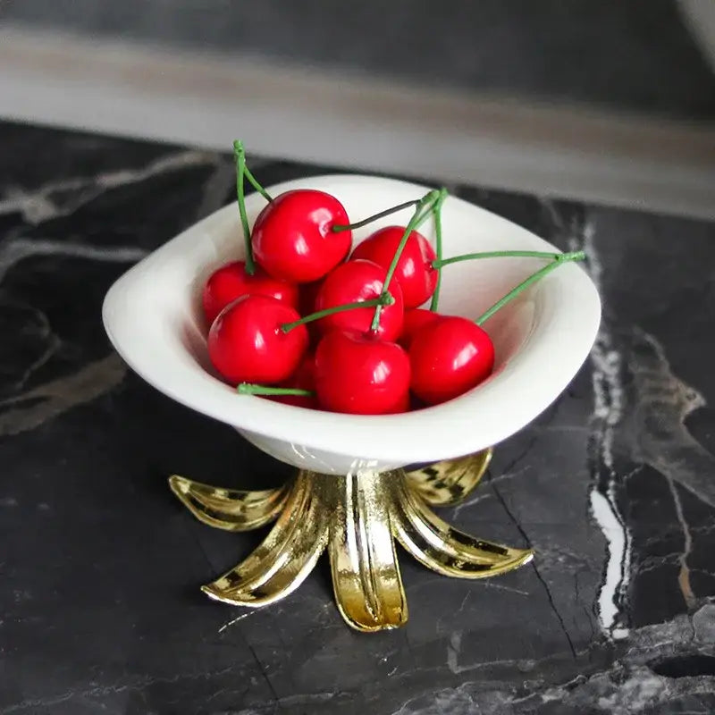 White and gold ceramic fruit plate bowl with gold leaf base filled with red cherries as dining room centerpiece