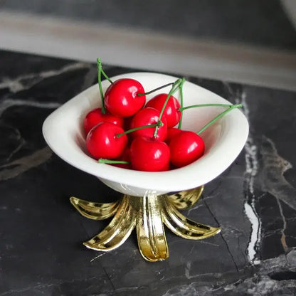 White and gold ceramic fruit plate bowl with gold leaf base filled with red cherries as dining room centerpiece