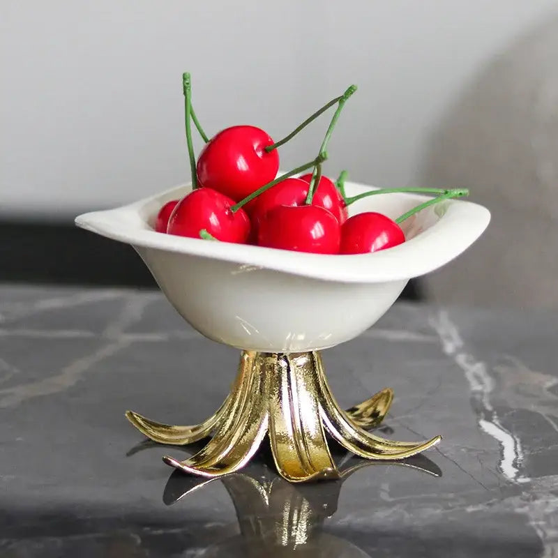 White ceramic fruit plate with gold leaf pedestal base filled with bright red cherries in a dining room centerpiece