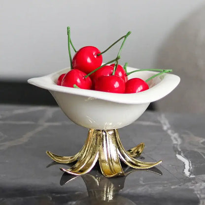 White ceramic fruit plate with gold leaf pedestal base filled with bright red cherries in a dining room centerpiece