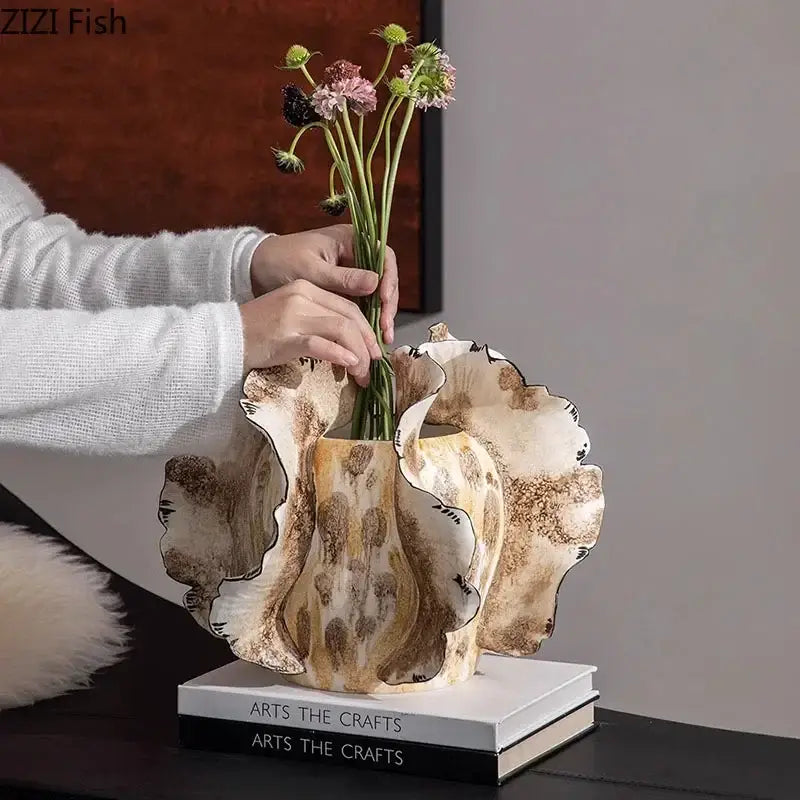 Creamy beige ceramic vase with a fluted ruffled rim and mottled brown glaze holding artificial flowers by decorbites colorful wings