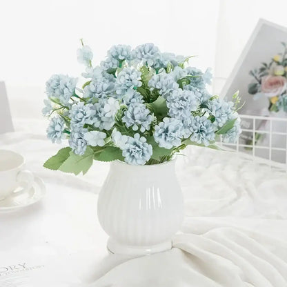 A delicate light blue artificial hydrangea bouquet with green leaves in a white ribbed ceramic vase for decorbites decor