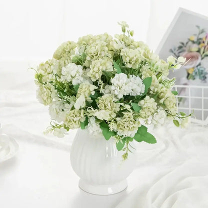 A decorbites hydrangea bouquet of artificial cream and white flowers with green foliage in a white ribbed glass vase
