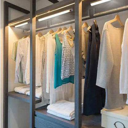 Modern gray wood-framed walk-in closet with white led motion sensor cabinet light illuminating neatly arranged clothing
