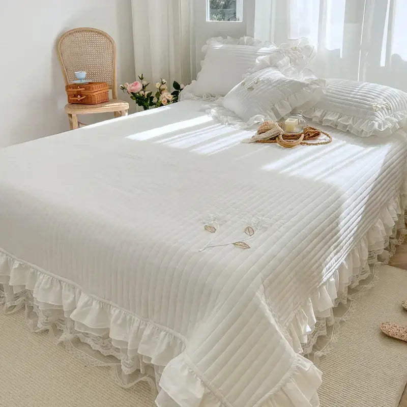 White quilted bedspread coverlet with delicate ruffled edges and embroidered leaf details for bedroom use