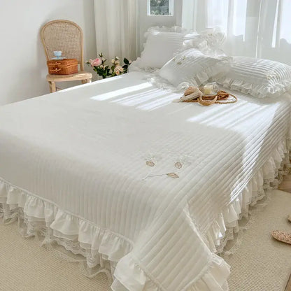 White quilted bedspread coverlet with delicate ruffled edges and embroidered leaf details for bedroom use