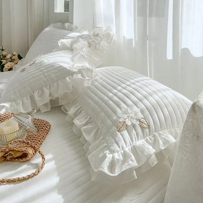 White quilted bedspread coverlet with ruffled edges and delicate embroidered floral appliqués for bedroom use