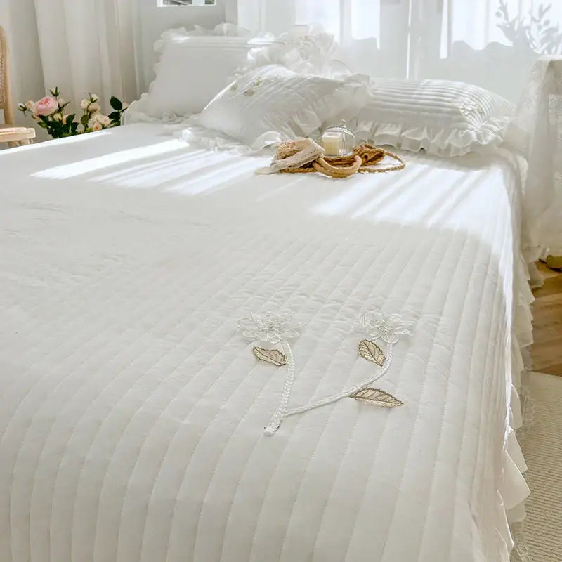 White quilted bedspread coverlet with delicate floral embroidery and ruffled edges for elegant bedroom decor