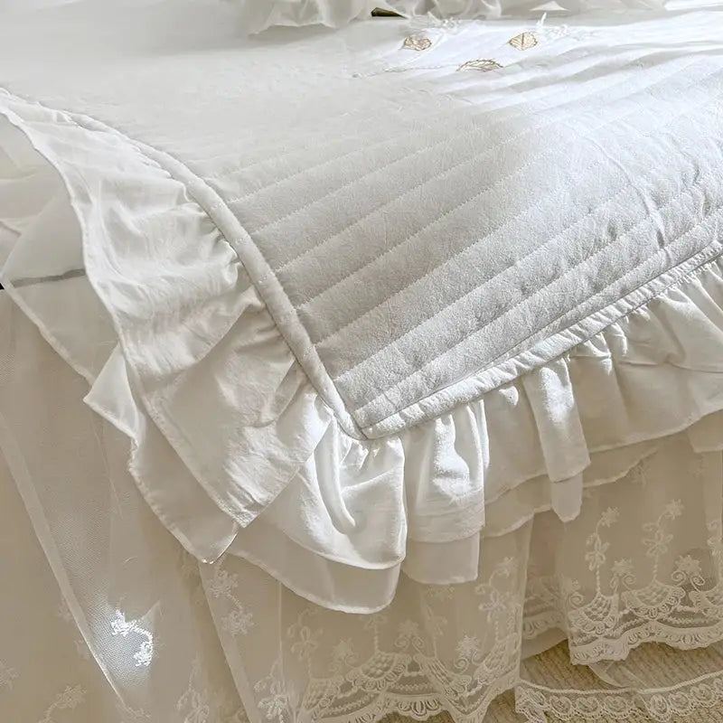 White quilted bedspread coverlet with ruffled edges and delicate lace embroidery for bedroom use