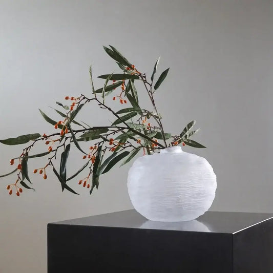 White textured ceramic glass pleats vase with rounded body and narrow neck holding green leaves and orange berries