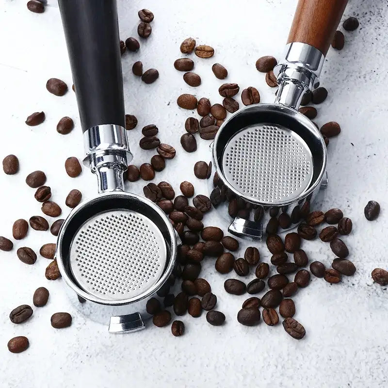 Two stainless steel coffee filters with wooden and black bottomless portafilter handles surrounded by roasted coffee beans