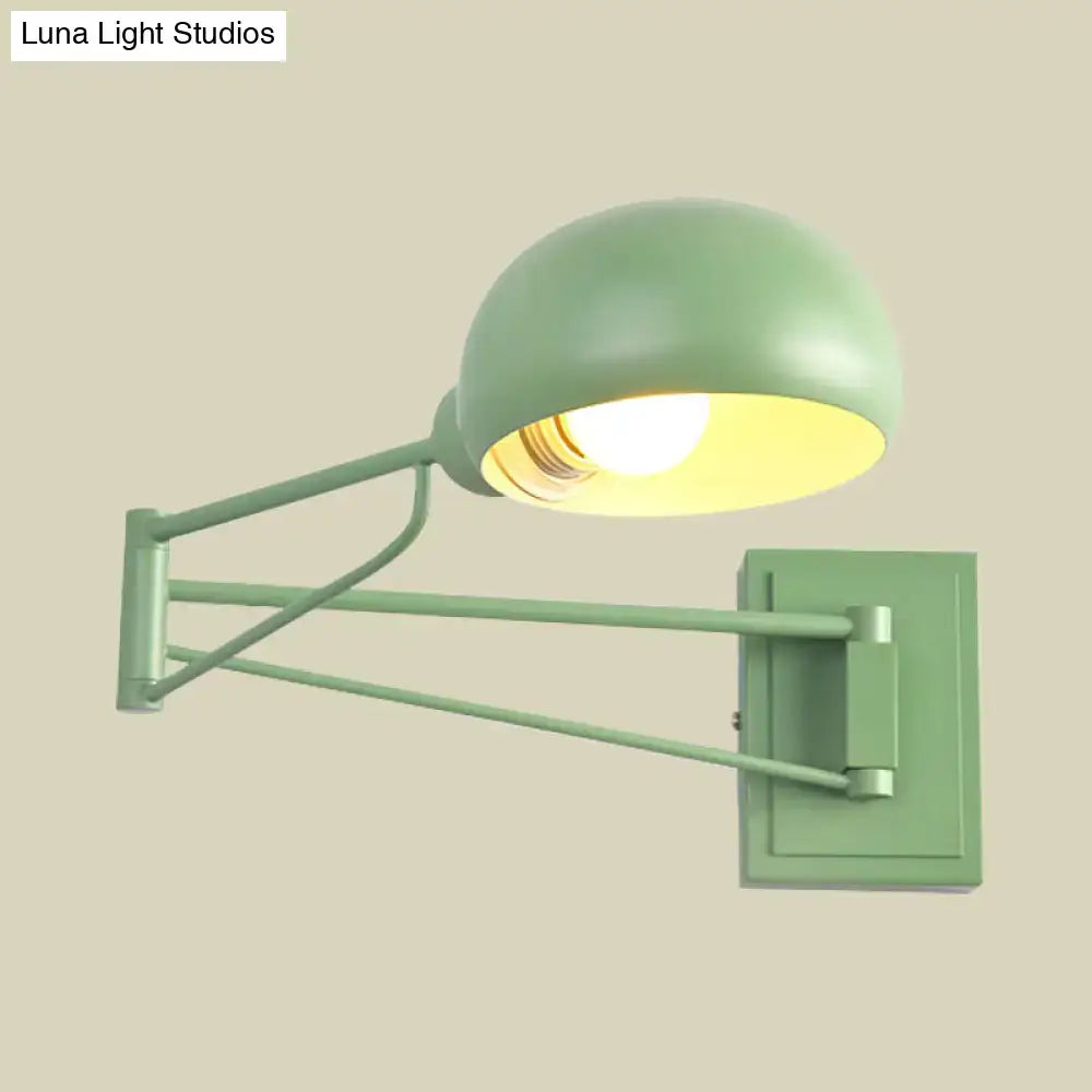 A matte sage green metal wall-mounted reading lamp with bowl shade and articulated arms for bedroom use