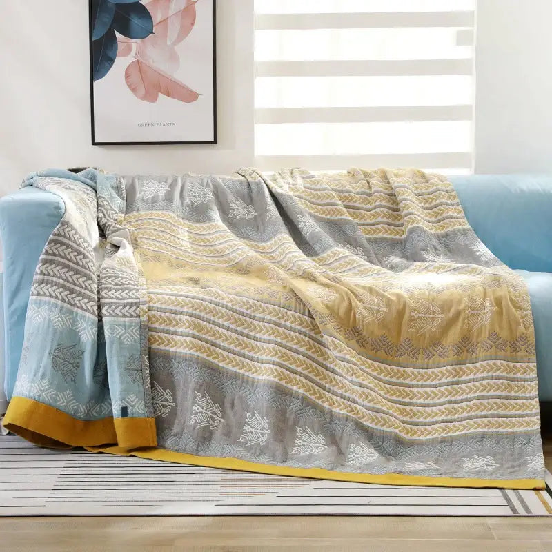 A soft cotton stripe gauze throw blanket in muted gray yellow and light blue with woven geometric designs for summer use