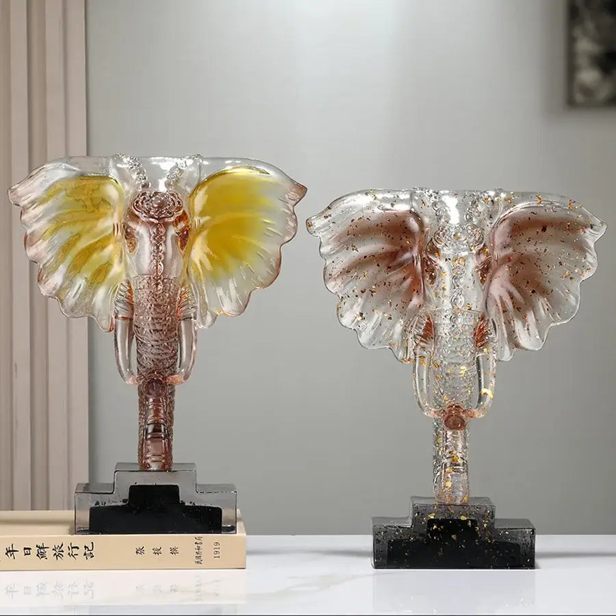 Two translucent yellow and blue decorbites crystal elephant sculptures with golden accents on black marble bases for home decor