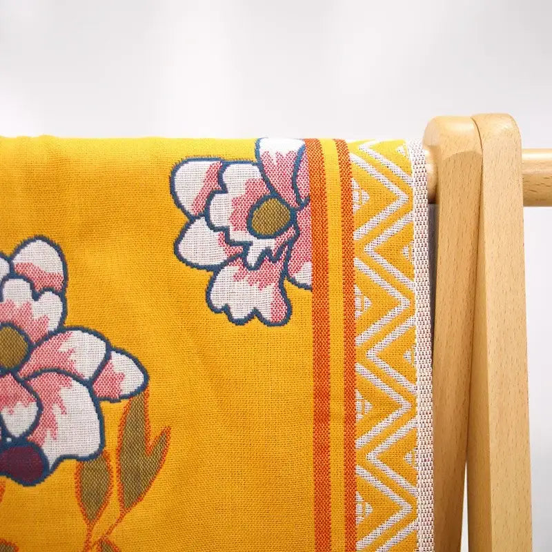 A vibrant yellow cotton large bath towel with embroidered pink and white flowers and orange striped zigzag border