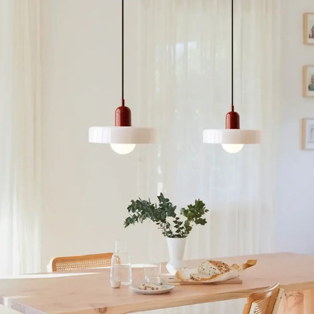 Two matte red cylindrical nordic canteen chandelier pendant lights with white shades hang over a wooden table