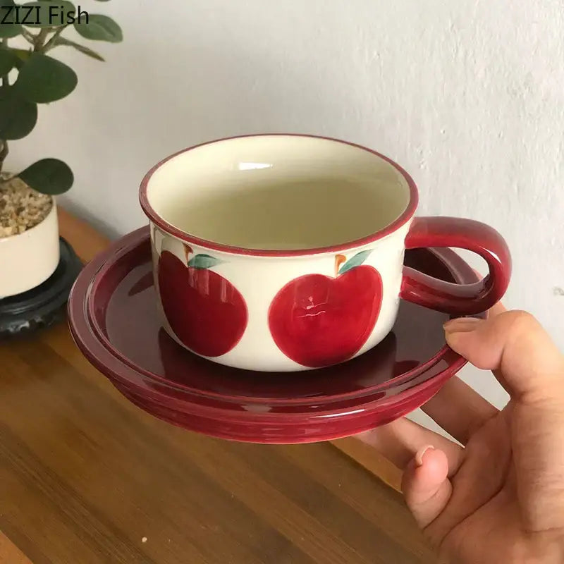 A white ceramic coffee mug with red apple fruits pattern porcelain and matching red rim on a deep-red saucer