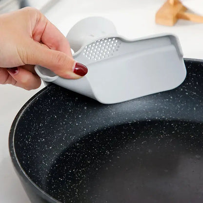Gray silicone pan scraper with perforated surface and ergonomic handle shown alongside yellow decorbites duck beak funnel